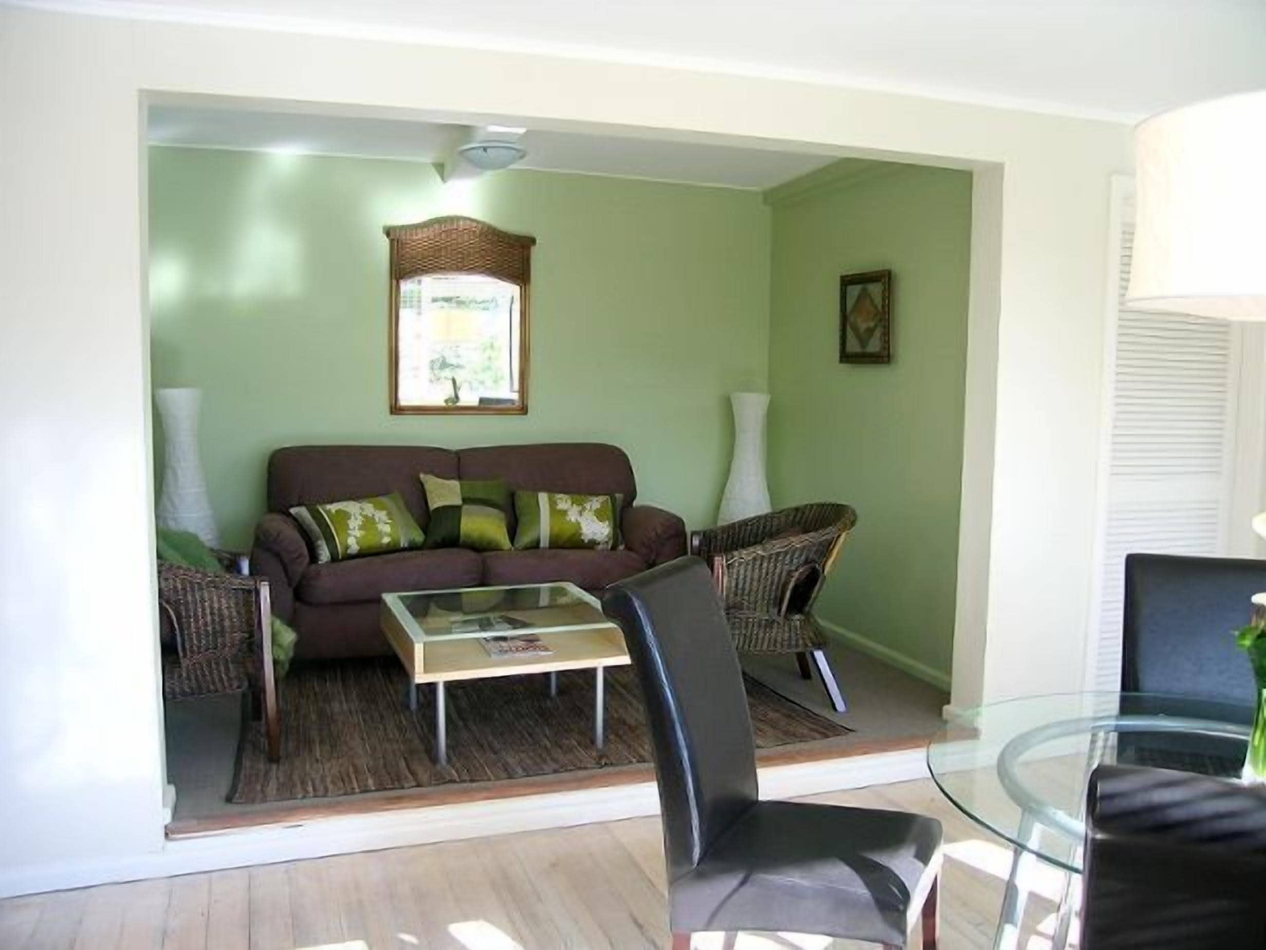 Ein Wohnzimmer mit braunem Sofa, einem Glastisch und Korbstühlen.