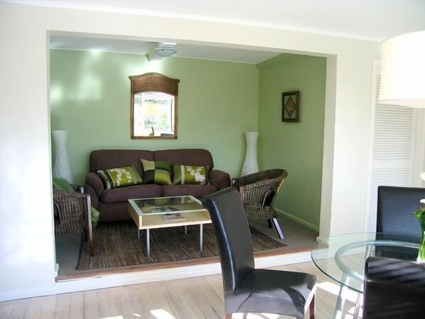 A living room with a brown sofa, a glass coffee table, and wicker chairs.