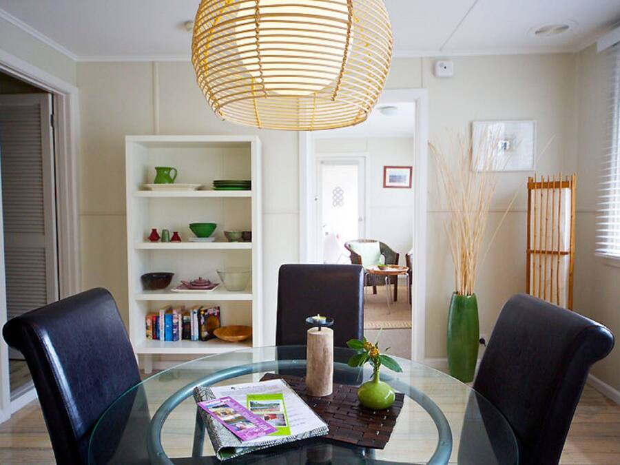 Un comedor con mesa de vidrio, dos sillas, una lámpara colgante y una estantería con diversos objetos.