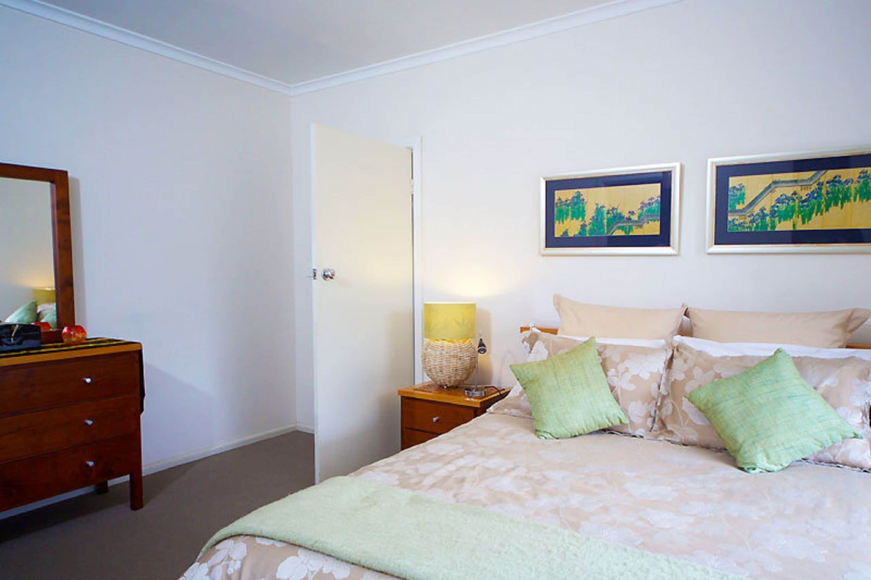 A bedroom with a bed, a nightstand, a dresser, and two framed pictures on the wall.
