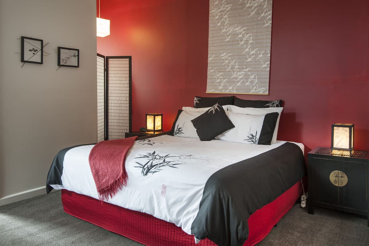 A neatly made bed with a red and black bedspread, two bedside lamps, and a wall-mounted light fixture.