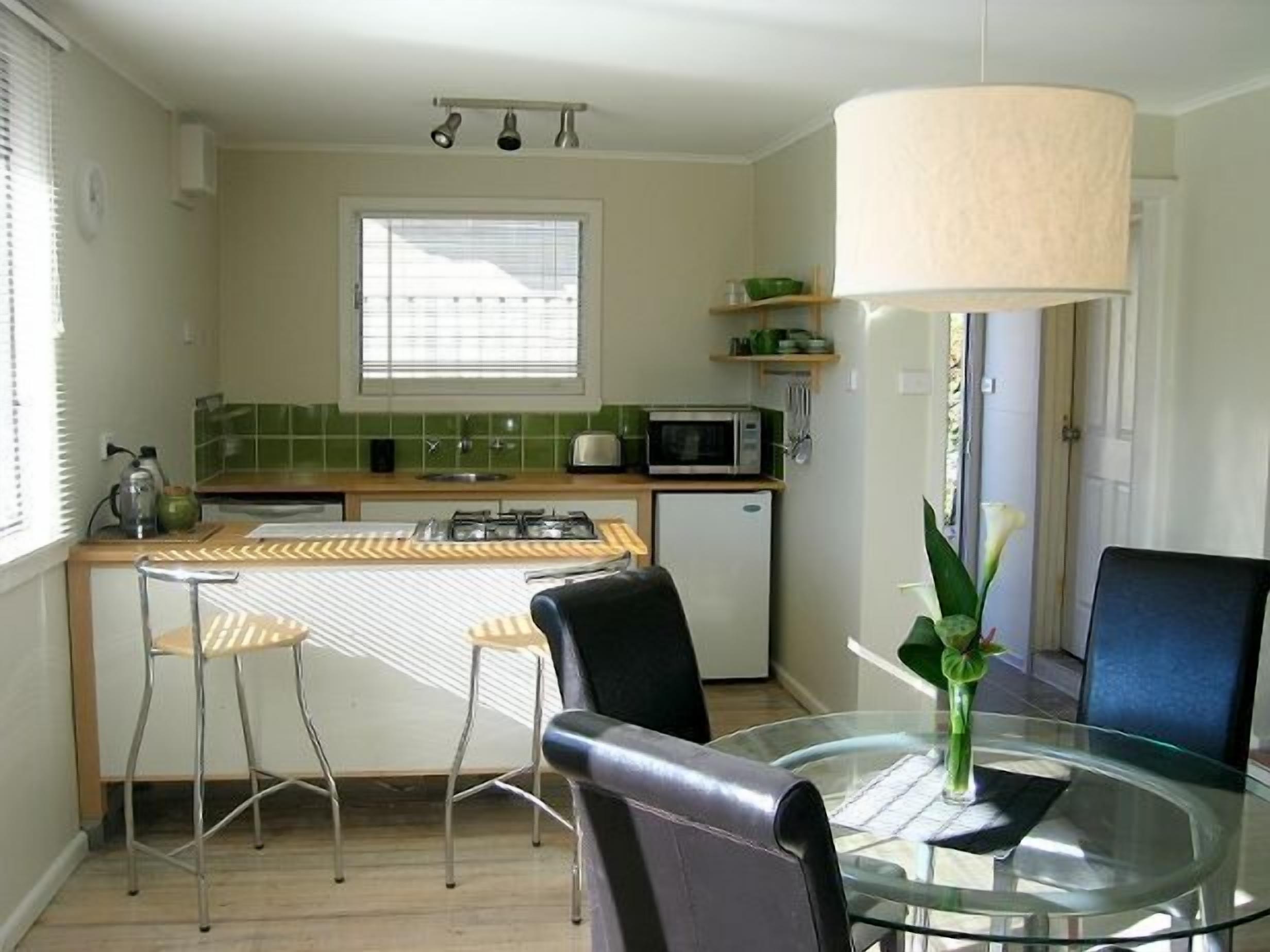 A compact kitchen with a central island, a dining area with a glass table, and a large window providing natural light.