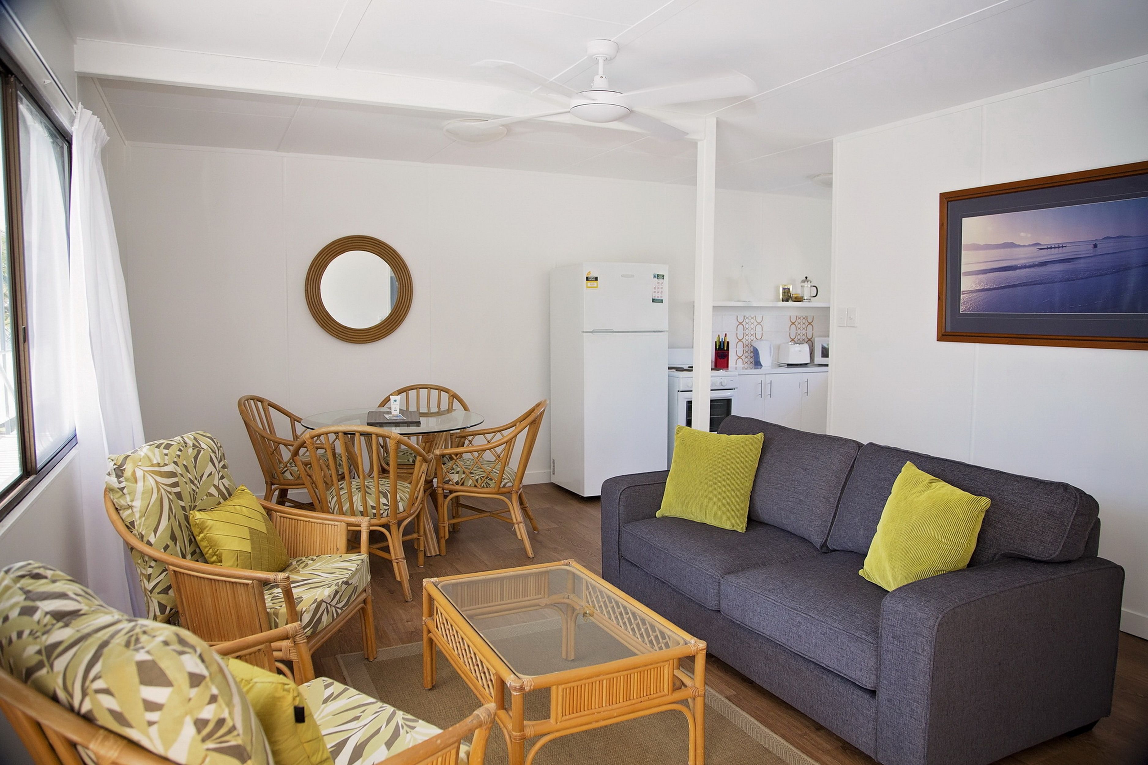 A living room with a grey sofa, two armchairs, a glass coffee table, and a dining table with chairs.