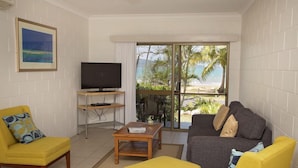 A living room with a TV, yellow armchairs, a gray sofa, and a view of the beach. - Apollo Jewel Beachfront Apartments (South Mission Beach)
