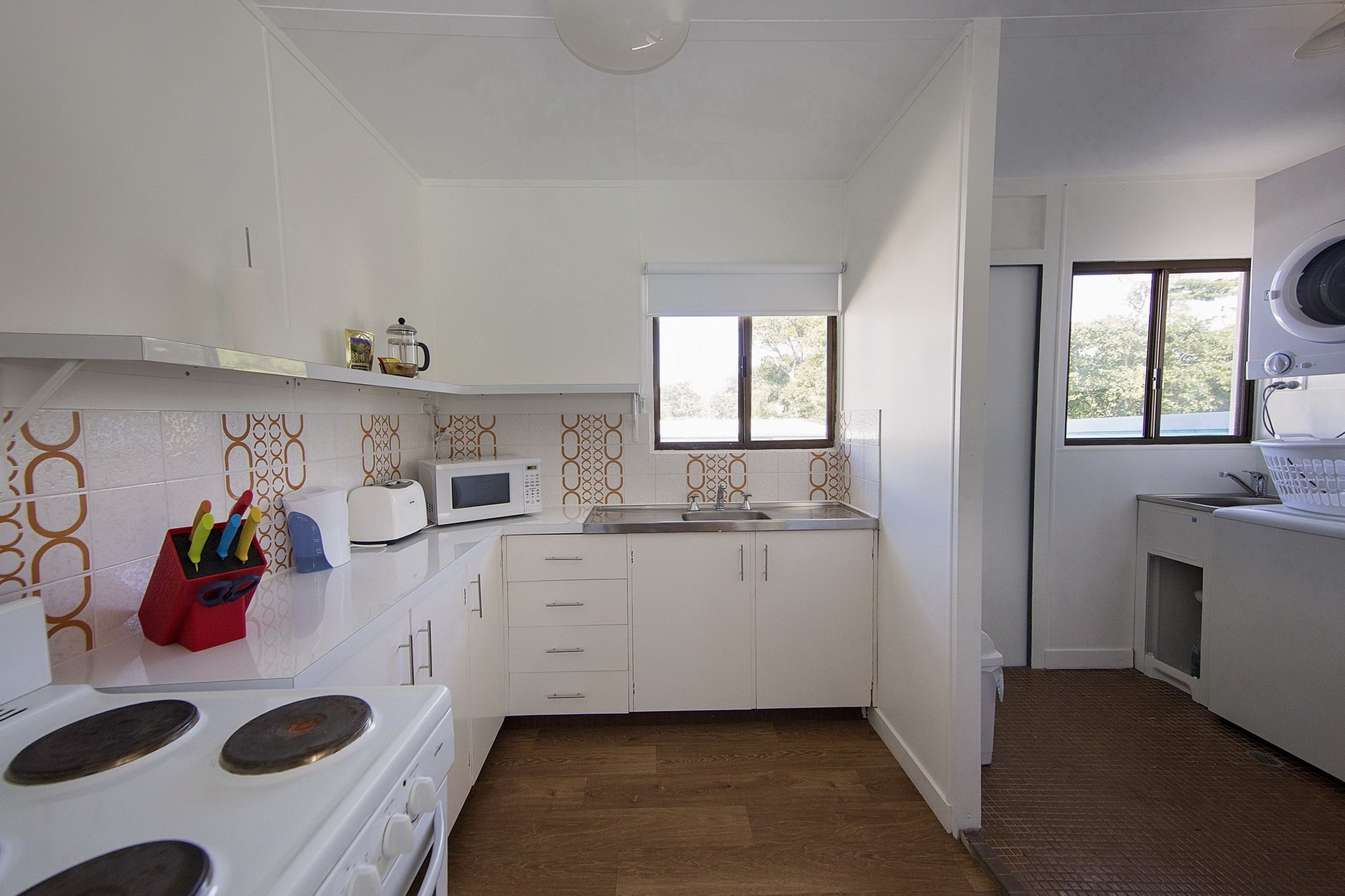 A compact kitchen with white cabinets, a microwave, a stove, and a window with blinds.