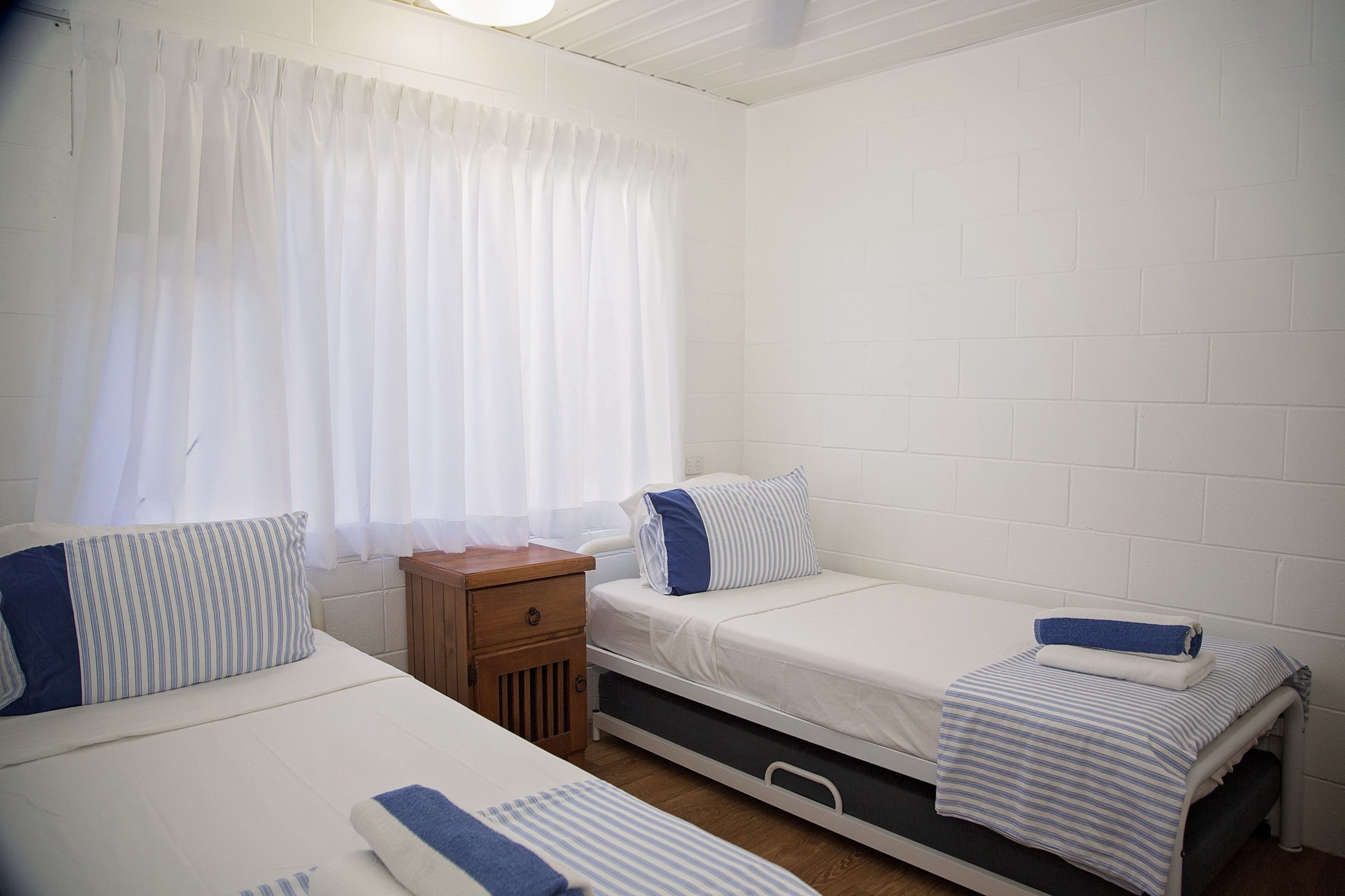 A small, clean room with two beds, a nightstand, and a window with curtains.