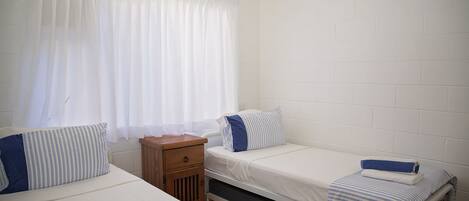 A small, clean room with two beds, a nightstand, and a window with curtains.