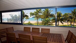 A wooden table and chairs in a room with large windows overlooking a beach with palm trees and the ocean. - Apollo Jewel Beachfront Apartments (South Mission Beach)