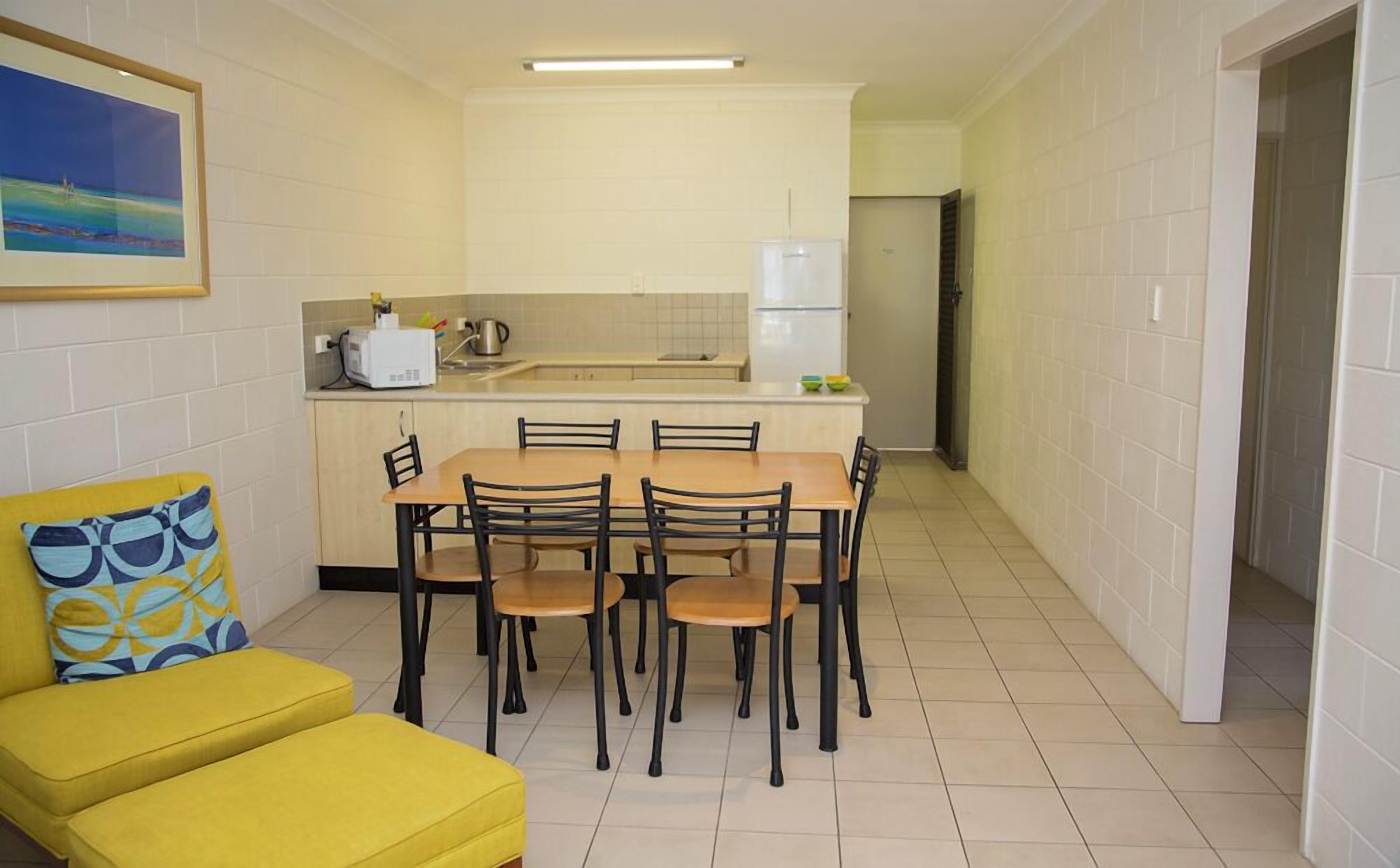 A compact kitchen with a dining area, a yellow sofa, and a painting on the wall.