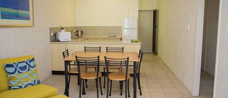 A compact kitchen with a dining area, a yellow sofa, and a painting on the wall.