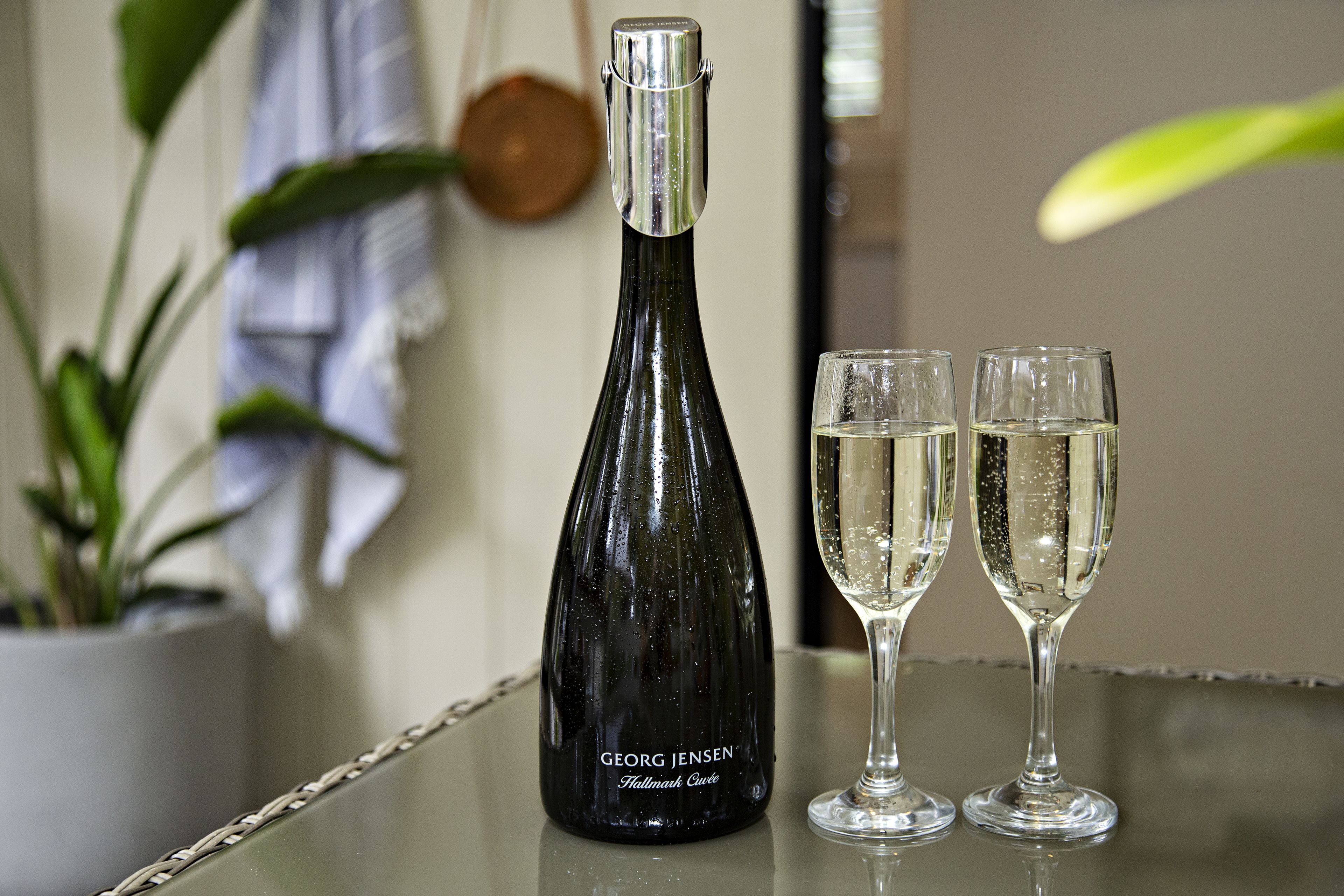 A bottle of Georg Jensen Hallmark Cuvée wine and two glasses on a reflective surface.