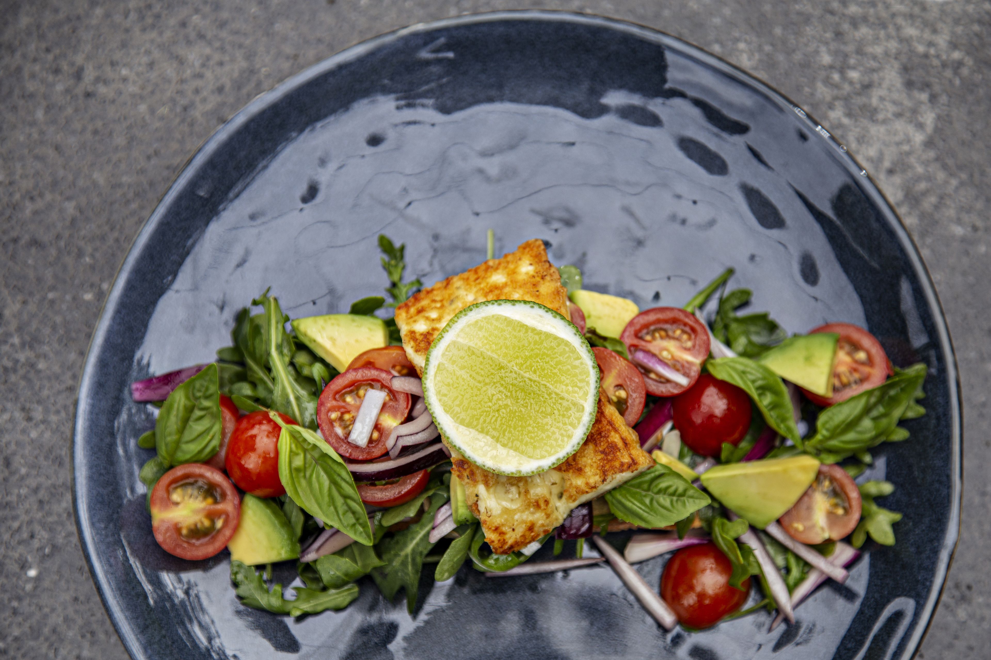 A plate of food with a slice of lime on top, surrounded by various vegetables and a piece of grilled chicken.