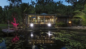 Una casa moderna con fachada de vidrio, un estanque con lirios y un muelle de madera.
