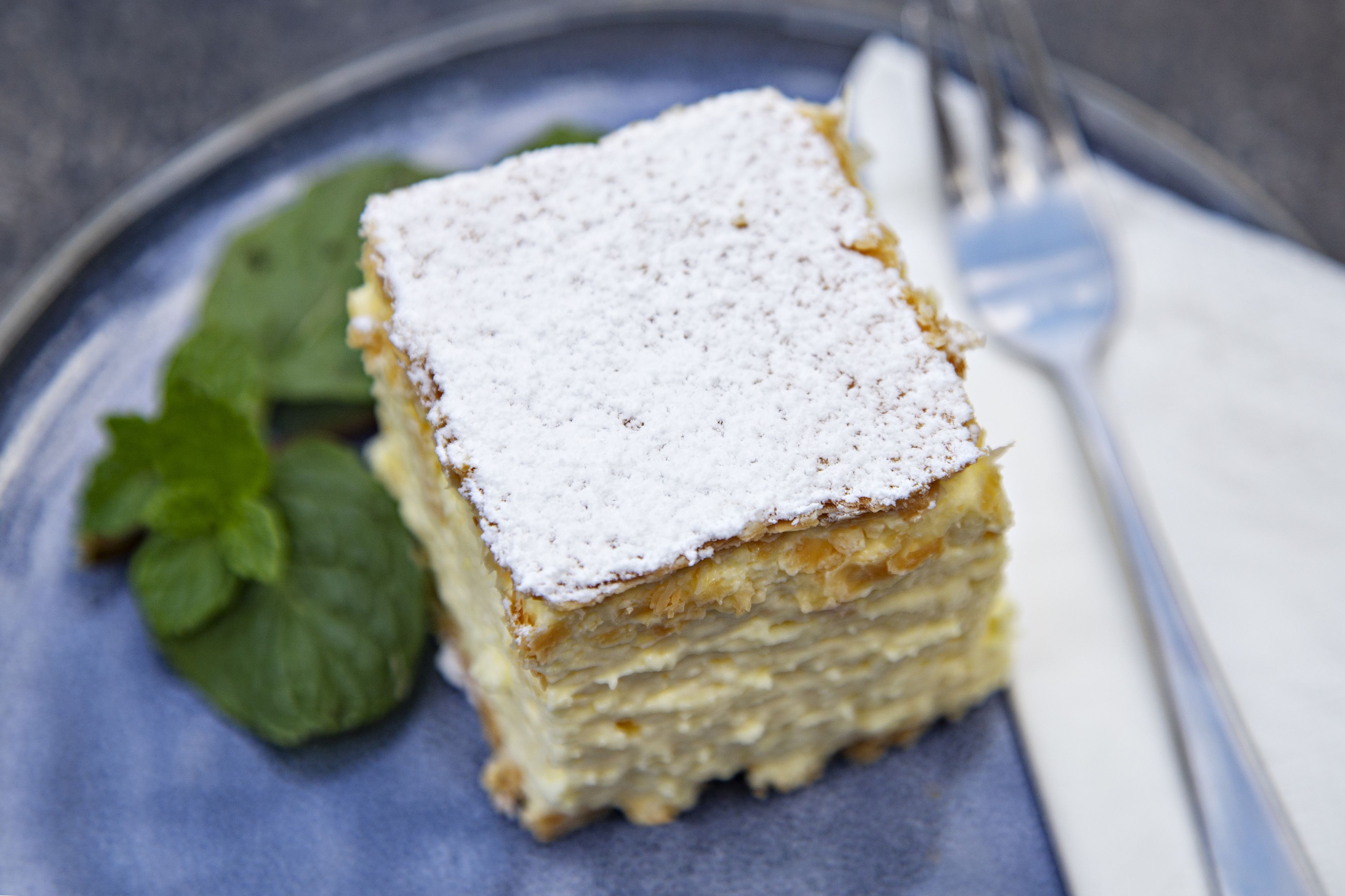 Un plato con postre en capas, un tenedor y hojas de menta a un lado.