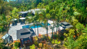 Vista aérea de un resort con piscina, áreas de descanso y vegetación tropical.