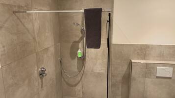 Douchegedeelte met een glazen deur, een handdouche en een shampoofles.