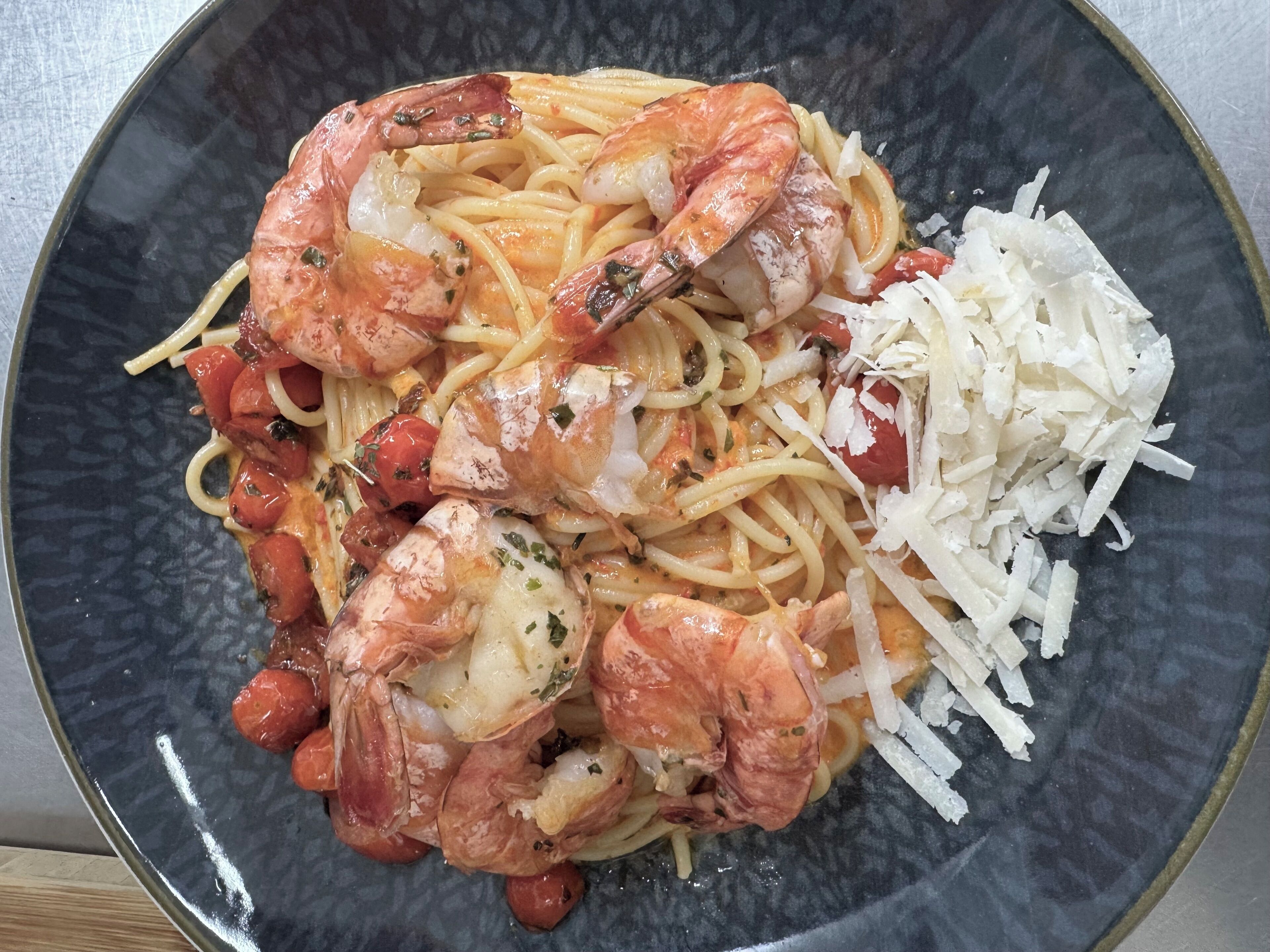 Un plato de espagueti con camarones, tomates y queso rallado.