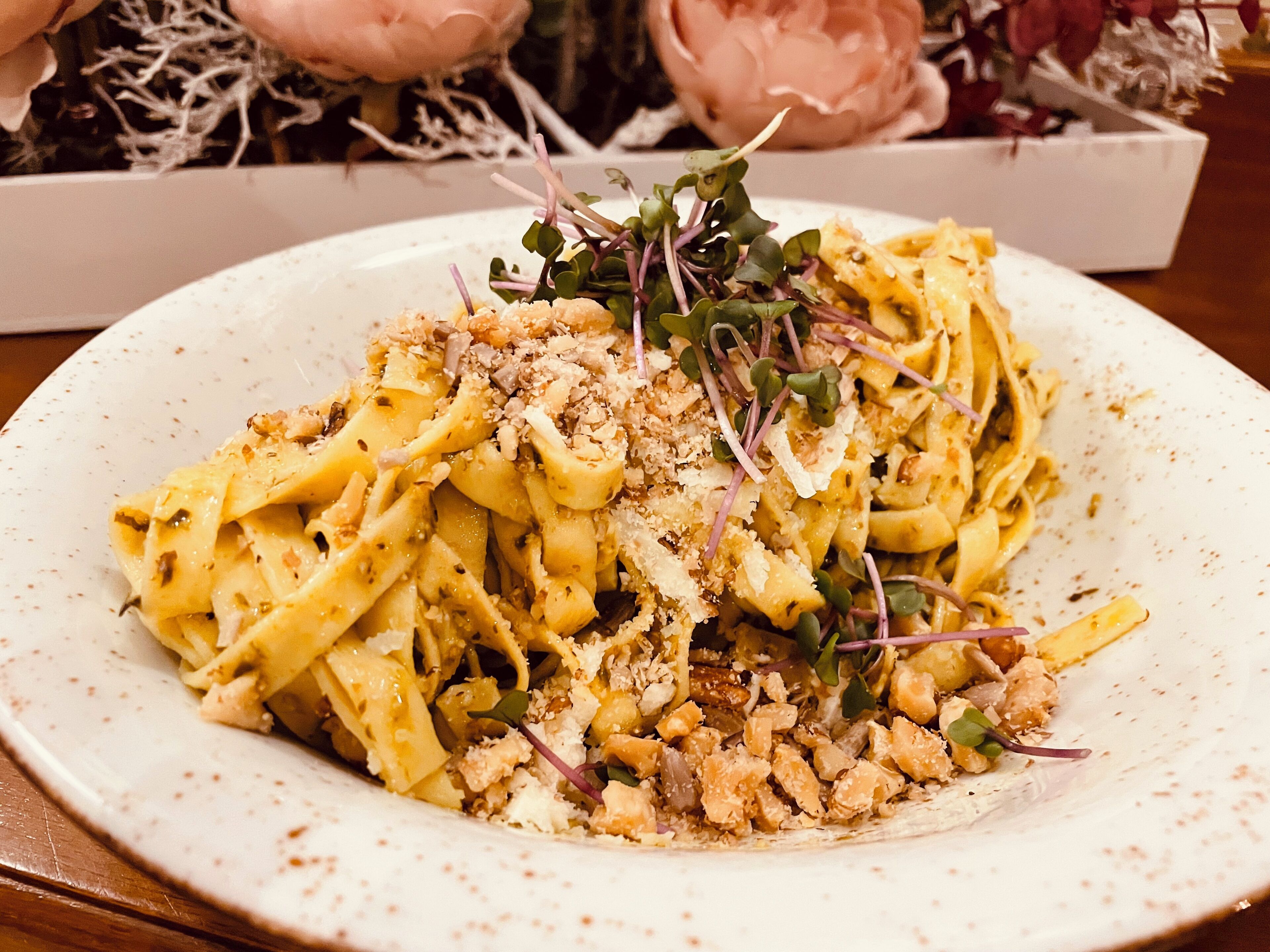 A plate of pasta with a creamy sauce, garnished with microgreens and crumbled cheese.