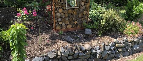 Un jardín con una estructura de madera rodeada por un muro de piedra, con diversas plantas y flores.
