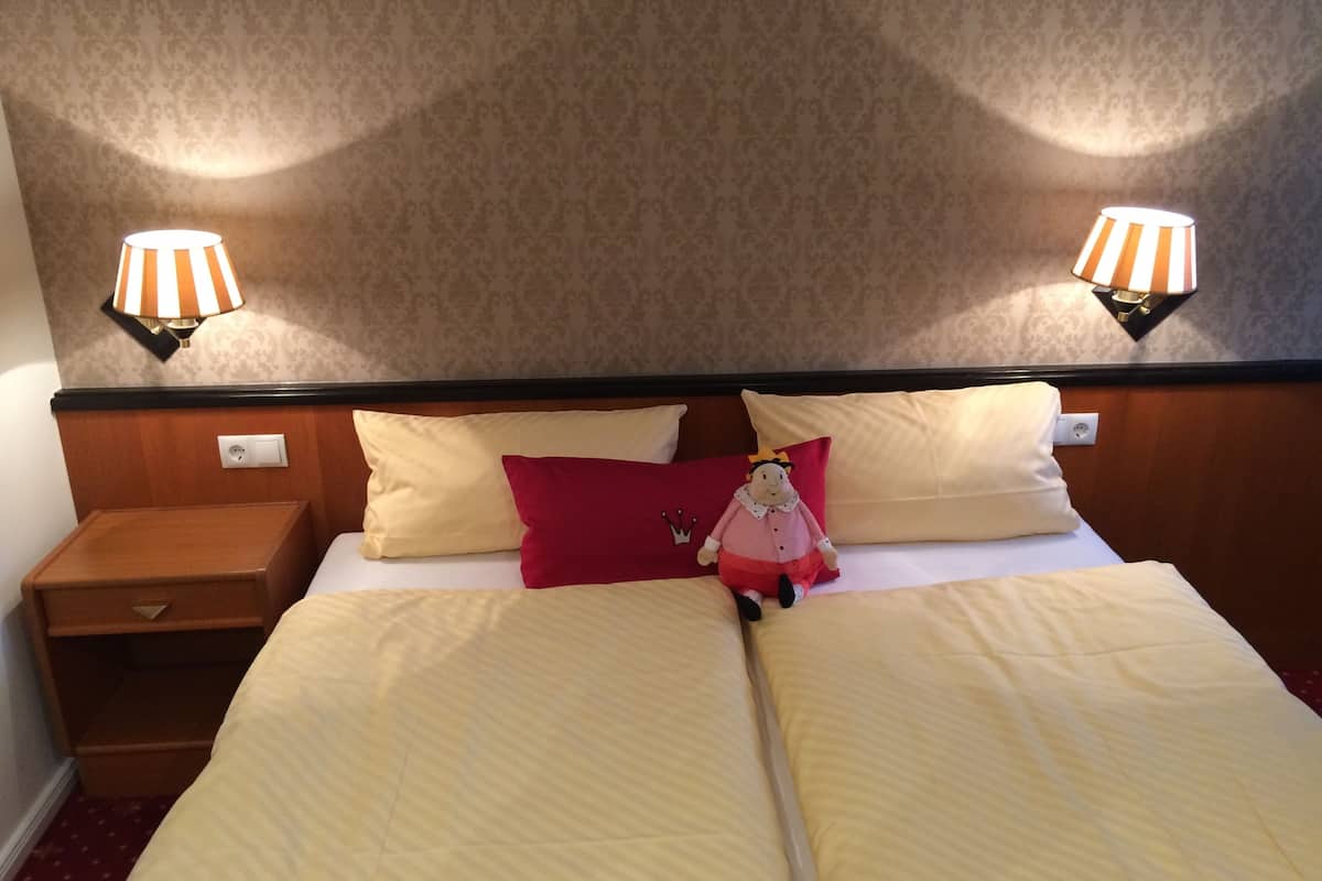 A hotel room with a double bed, two bedside lamps, a nightstand, and a decorative pillow.