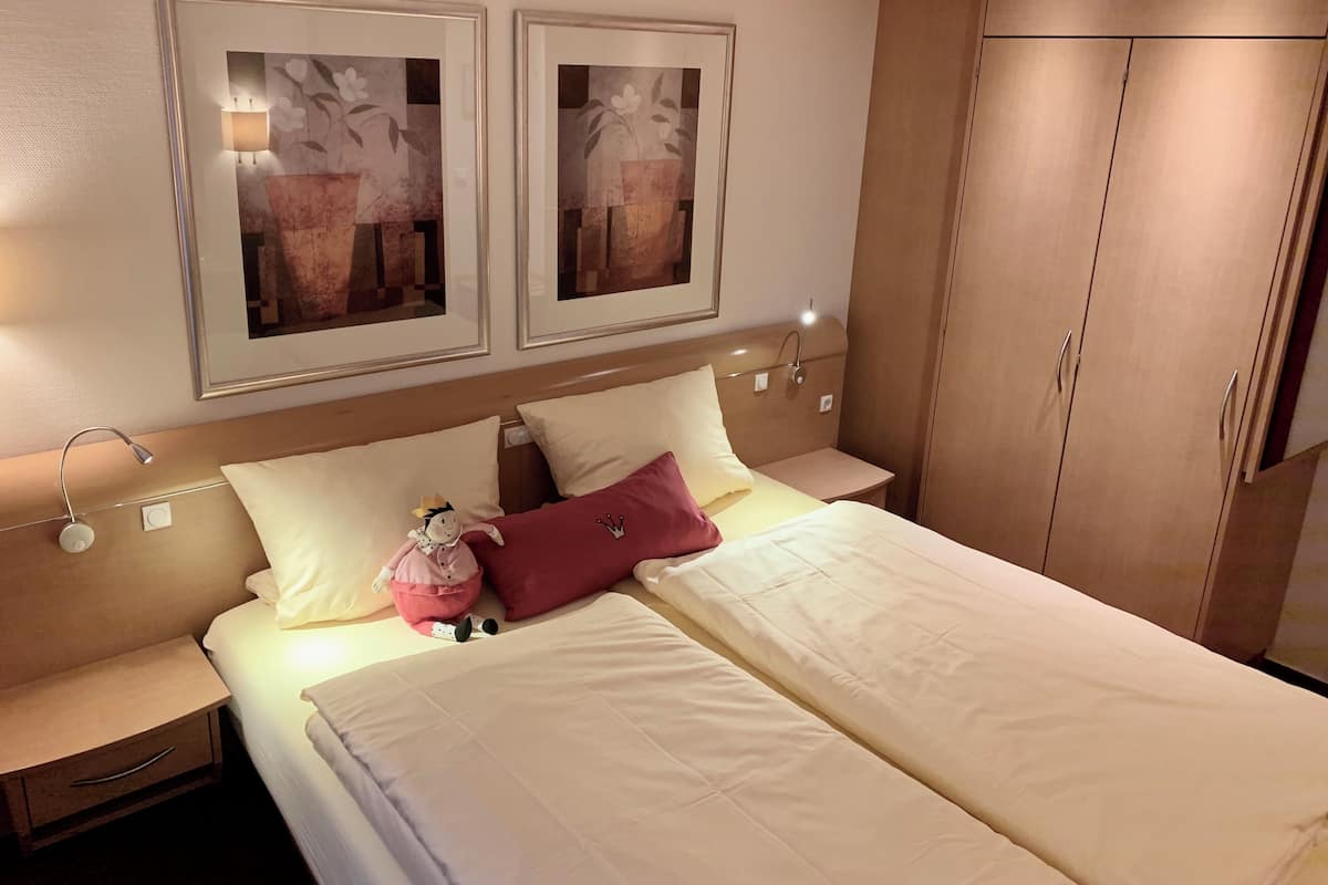 A neatly made bed with white and pink bedding, two wall-mounted lamps, and a wardrobe with sliding doors.