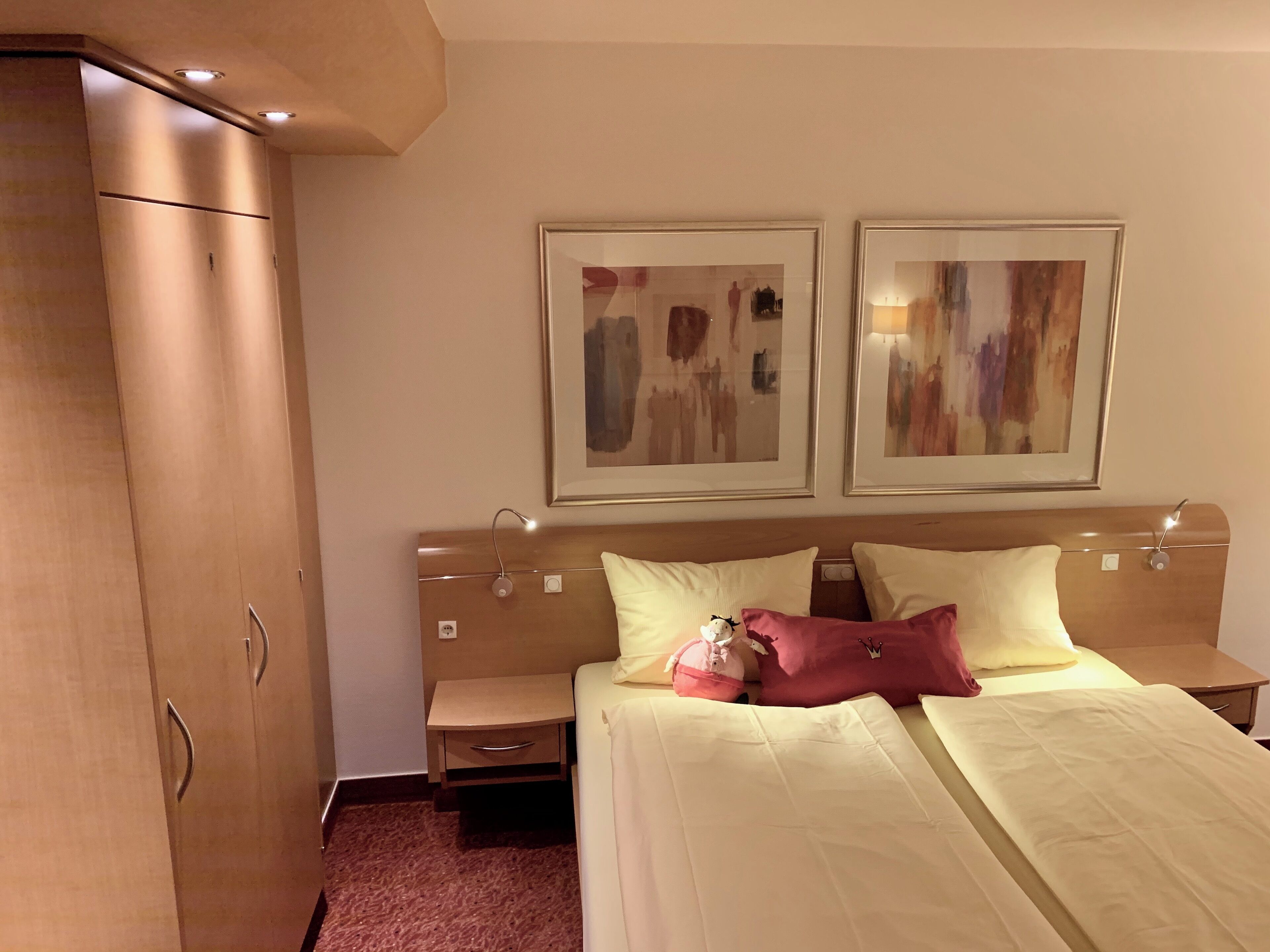 Quarto de hotel com cama, mesas de cabeceira, guarda-roupa e duas pinturas abstratas na parede.