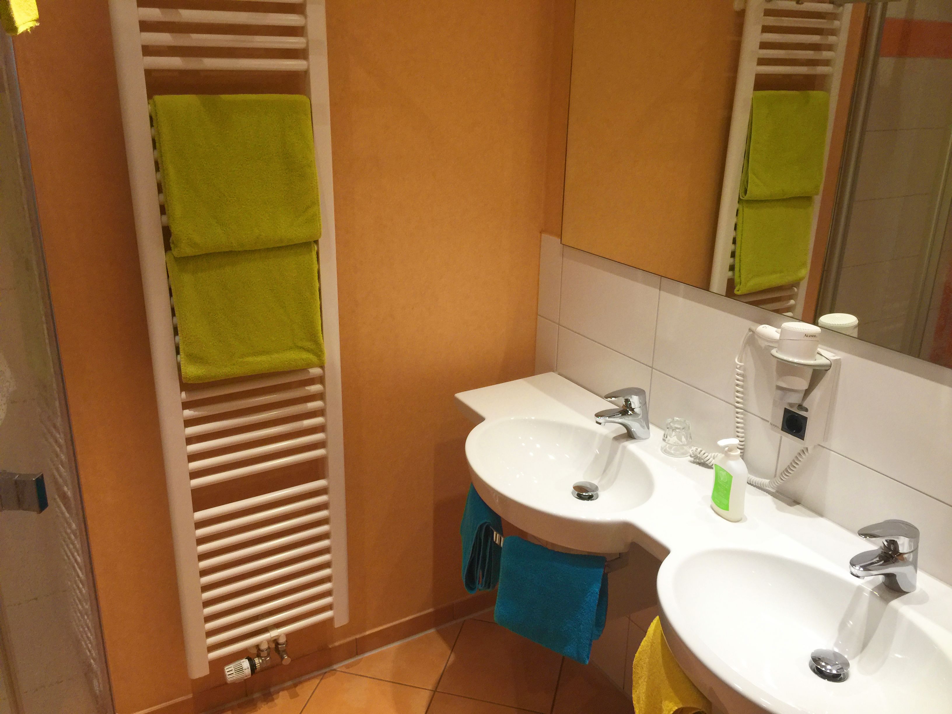 Un baño con dos lavamanos, un espejo y un perchero con toallas verdes.