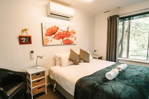 A neatly arranged hotel room with a bed, a side table with a lamp, a small picture frame, and a large floral painting on the wall.
