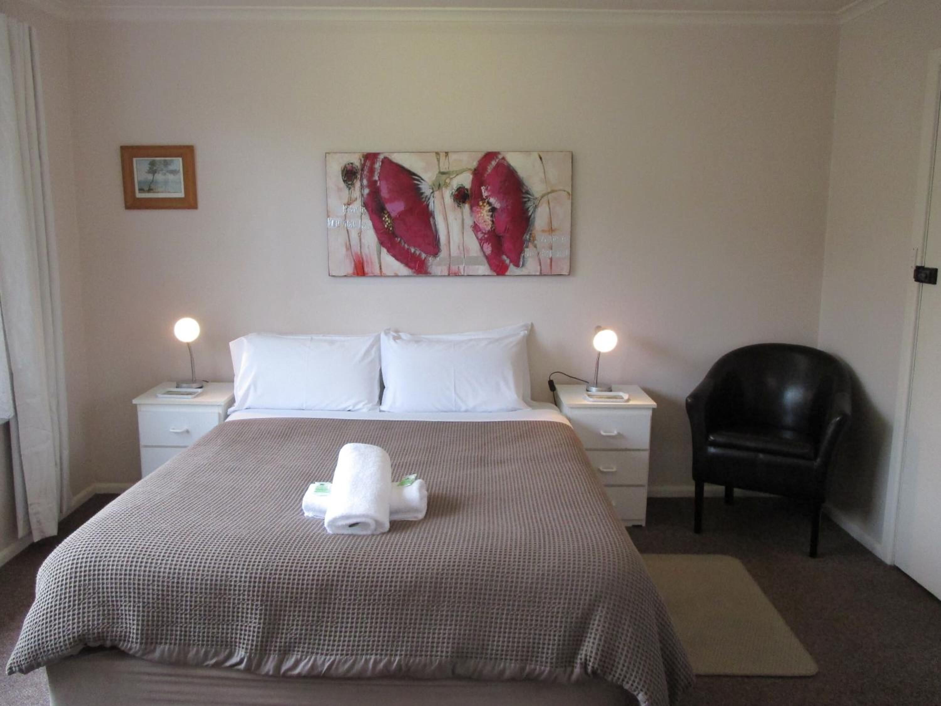 A hotel room with a bed, two bedside tables, a chair, and a painting on the wall.