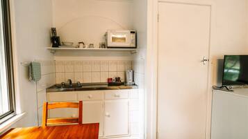 A compact kitchen with white cabinets, a microwave, a coffee maker, and a television on a stand.