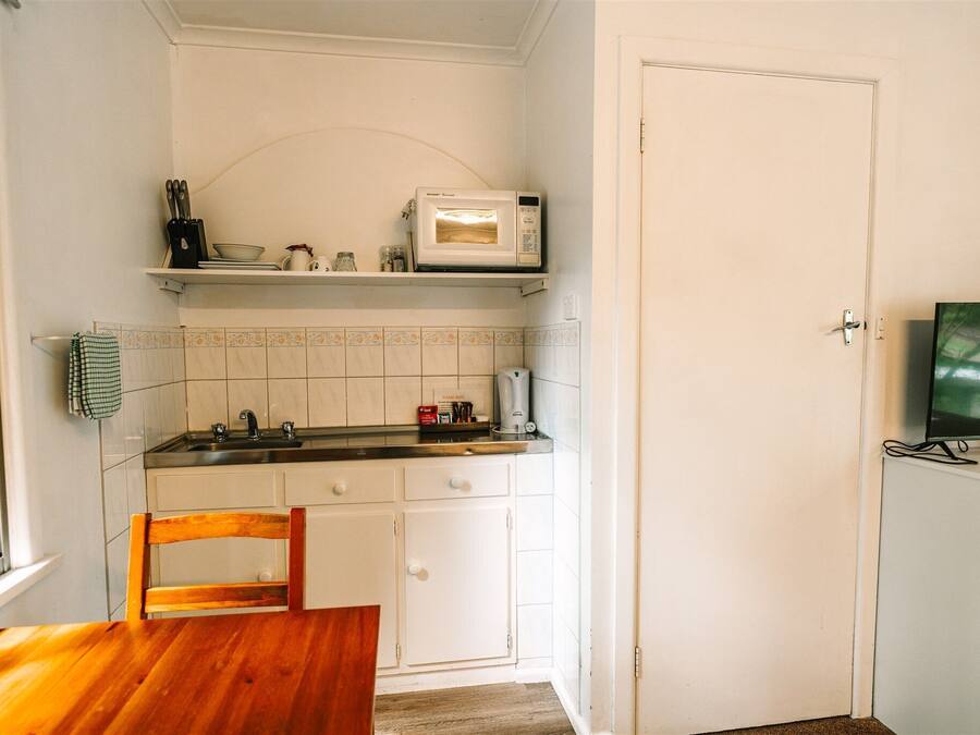 A compact kitchen with white cabinets, a microwave, a coffee maker, and a television on a stand.