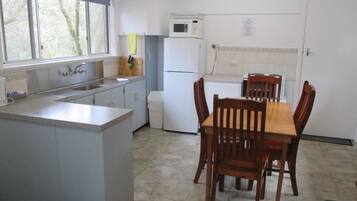 A compact kitchen with a central island, a dining table with chairs, a refrigerator, a microwave, and a window with a view of trees.