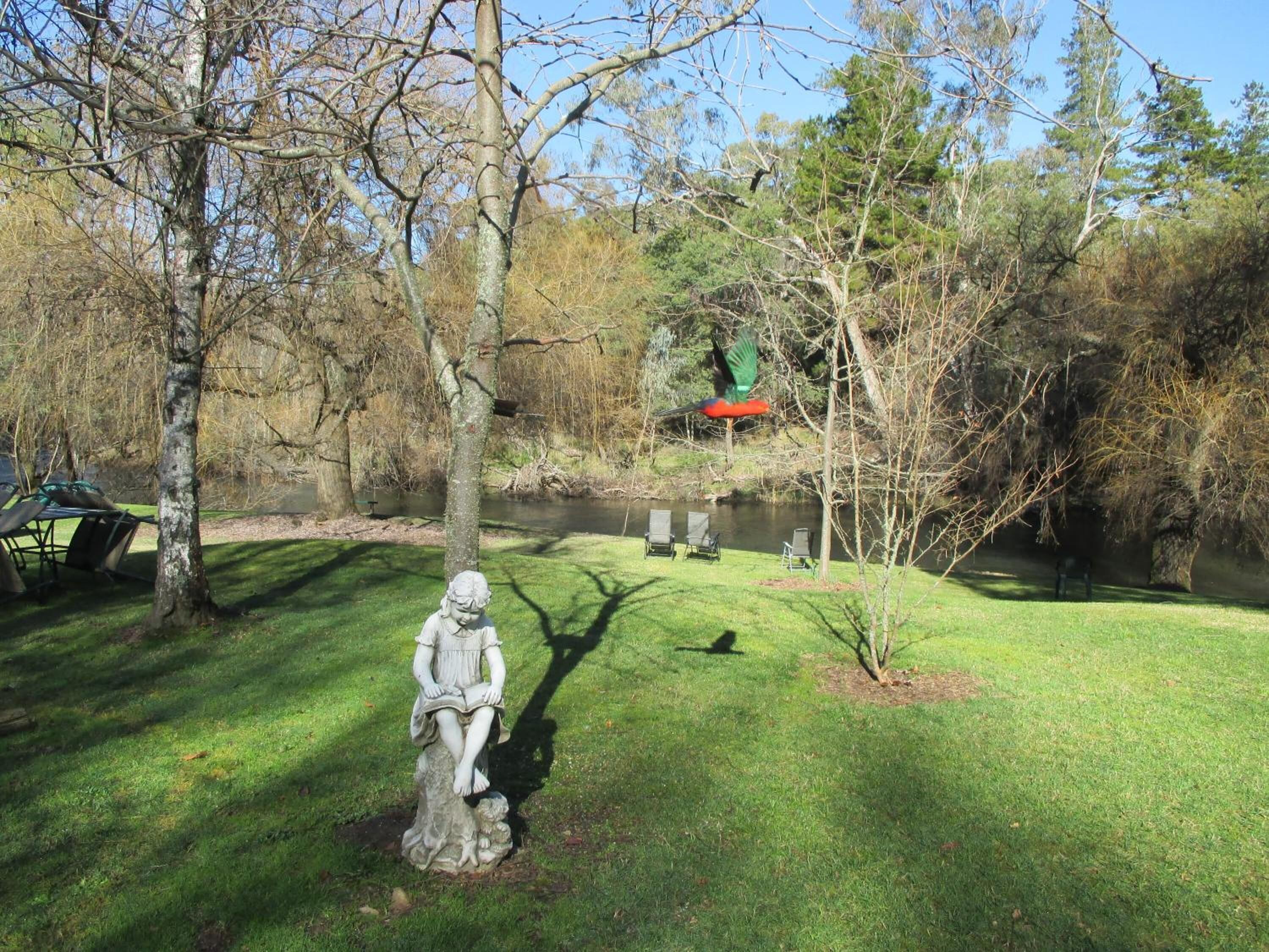 A statue of a seated figure in a park with a river and trees in the background.