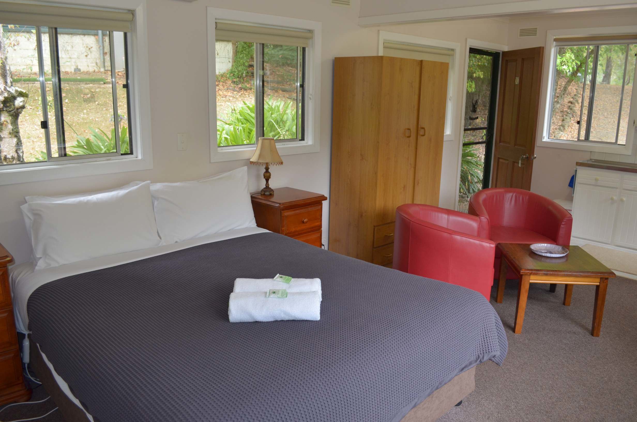 Una habitación de hotel con una cama grande, una silla roja, un armario de madera y una mesita con un bol.