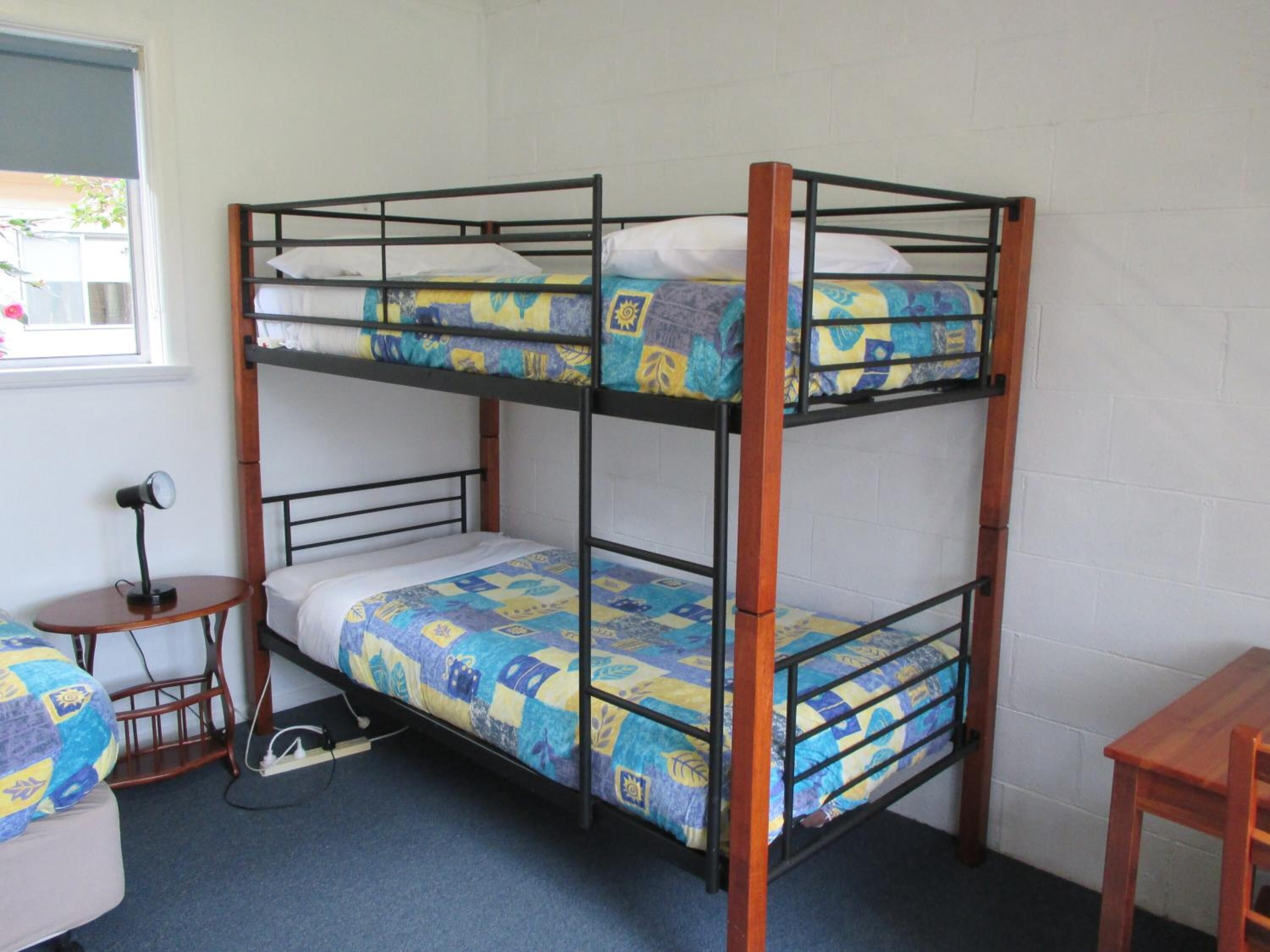 A bunk bed room with a desk and chair, a lamp, and a window.