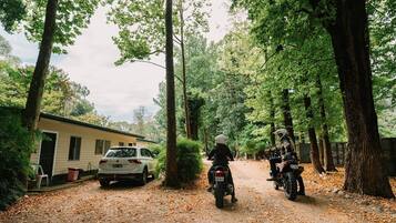 Un chemin de terre avec deux motos garées sur le bord, une voiture blanche et une caravane dans une zone boisée.