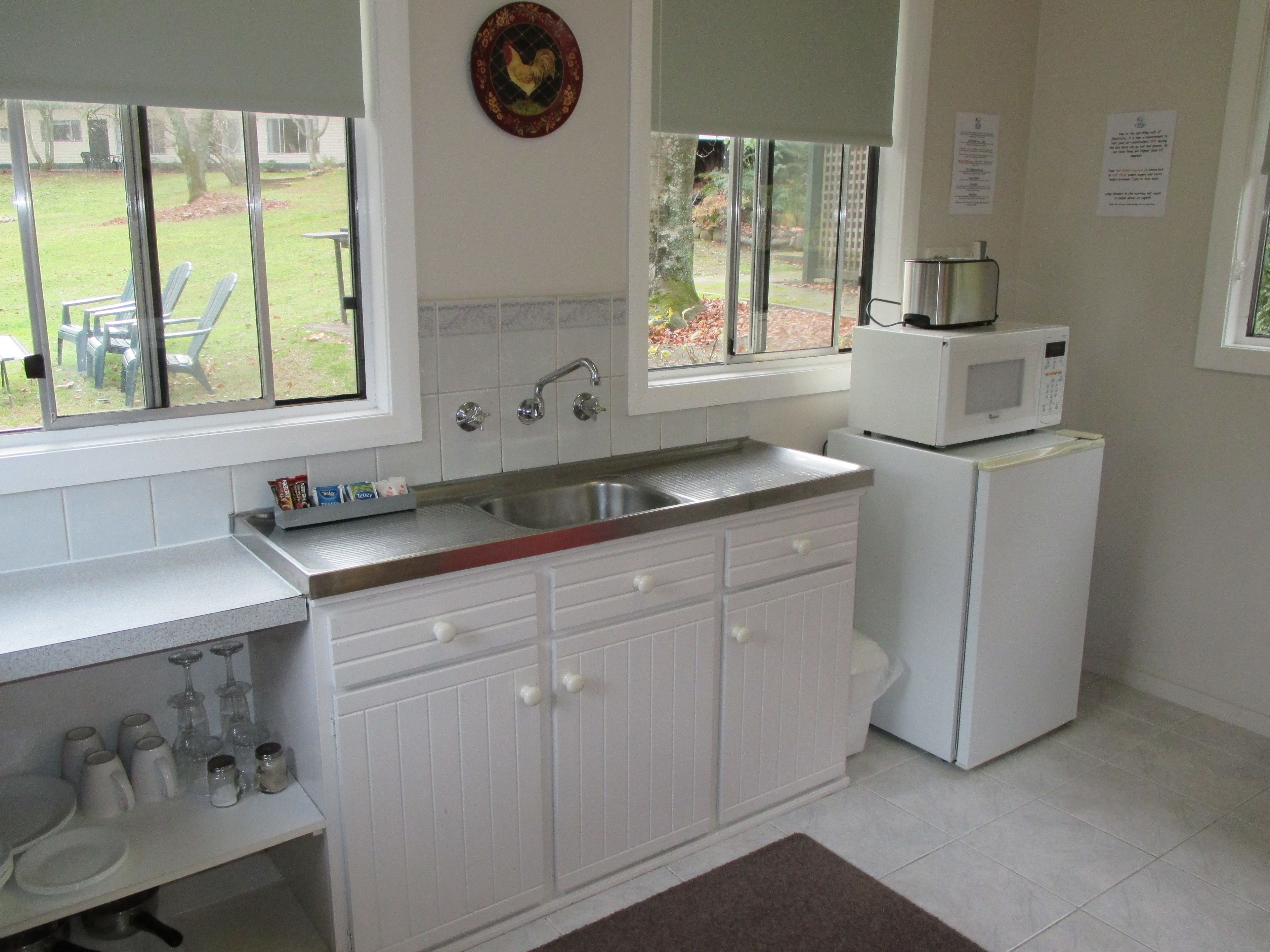 A kitchen with white cabinets, a stainless steel sink, and a microwave on top of a refrigerator.