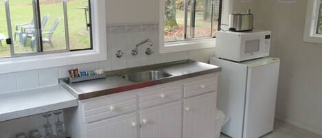 A kitchen with white cabinets, a stainless steel sink, and a microwave on top of a refrigerator.