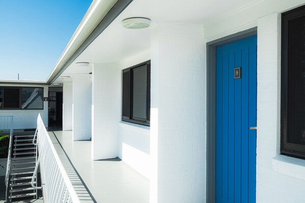 A modern building with white walls and a blue door, featuring a metal railing and a window. - Montego Mermaid Beach Motel (Mermaid Beach)