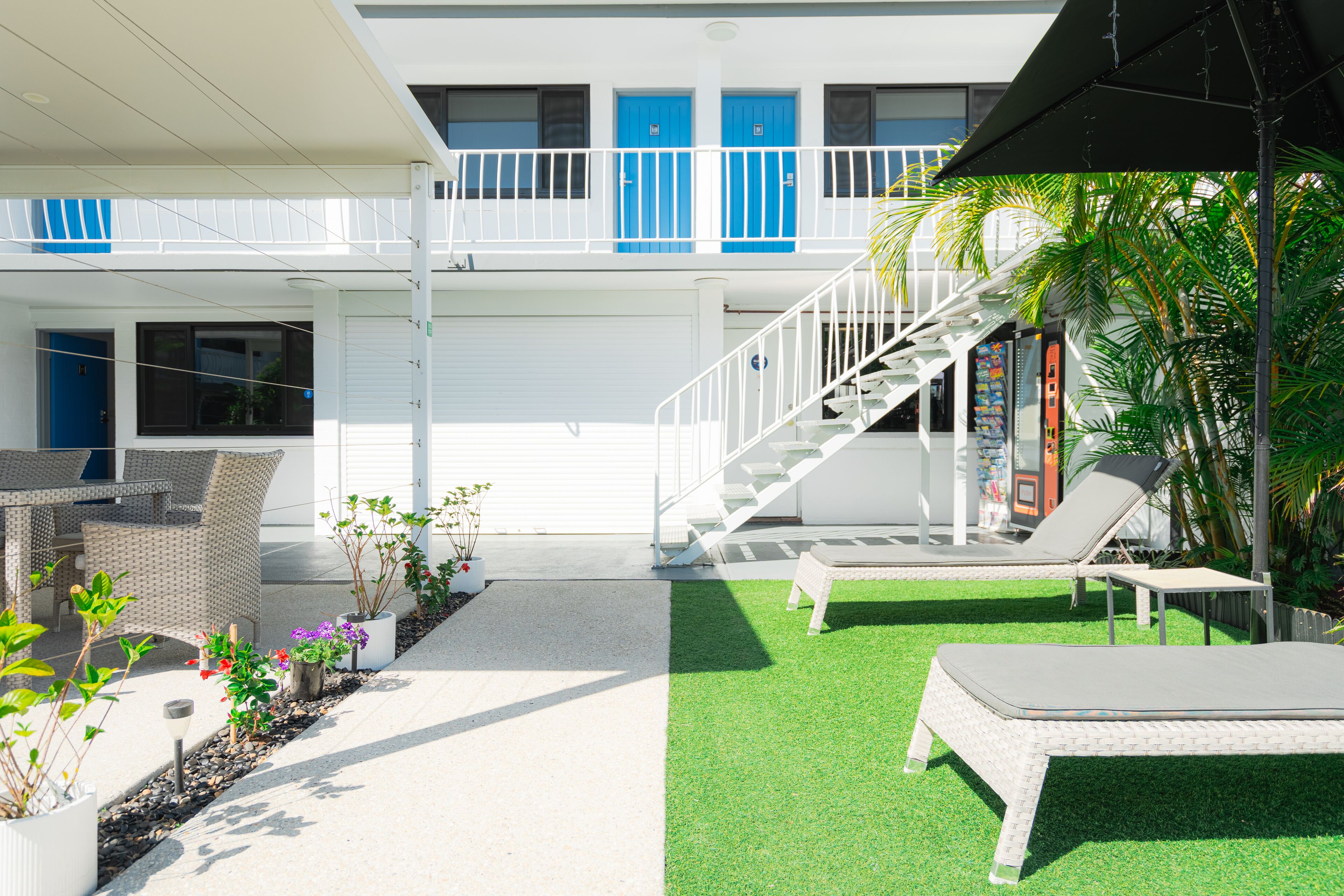 Un hotel con un área exterior techada, una escalera y sillones de relax sobre césped artificial.