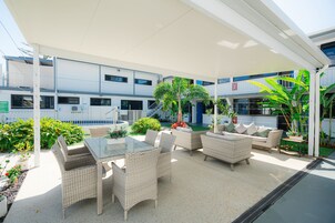 Un patio al aire libre con mobiliario de mimbre, una mesa de vidrio y plantas en macetas.