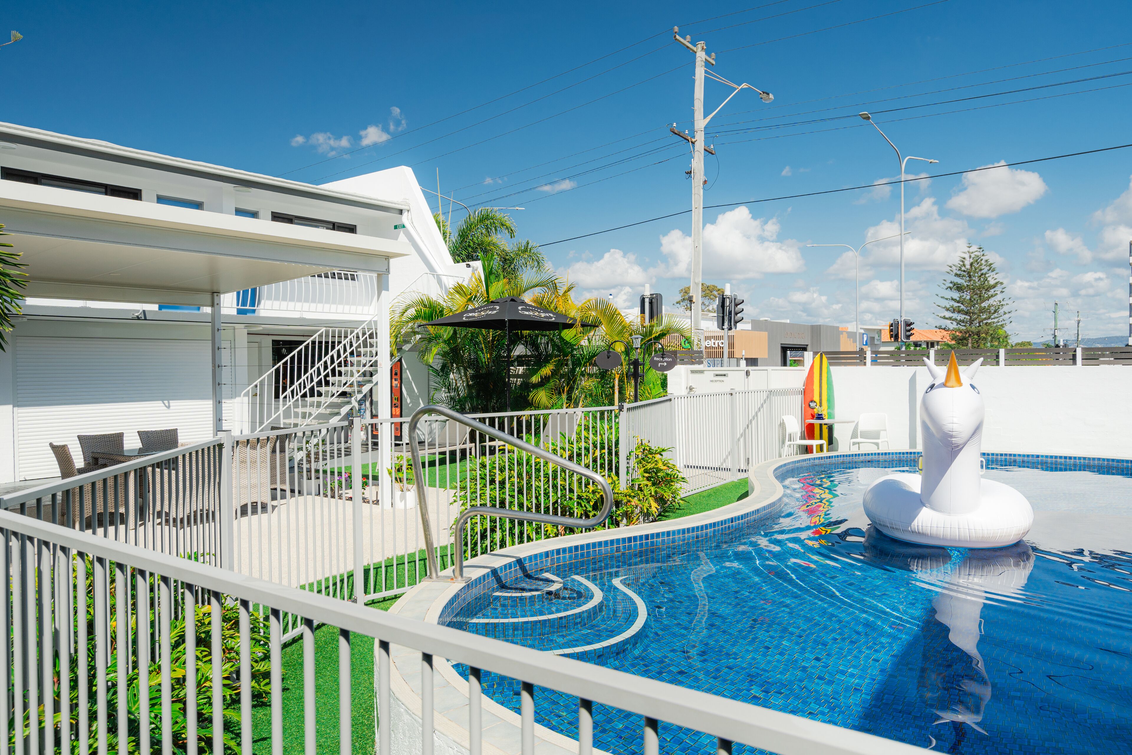 Una piscina con una estructura hinchable blanca, un área de descanso cubierta y una escalera que conduce a un edificio.
