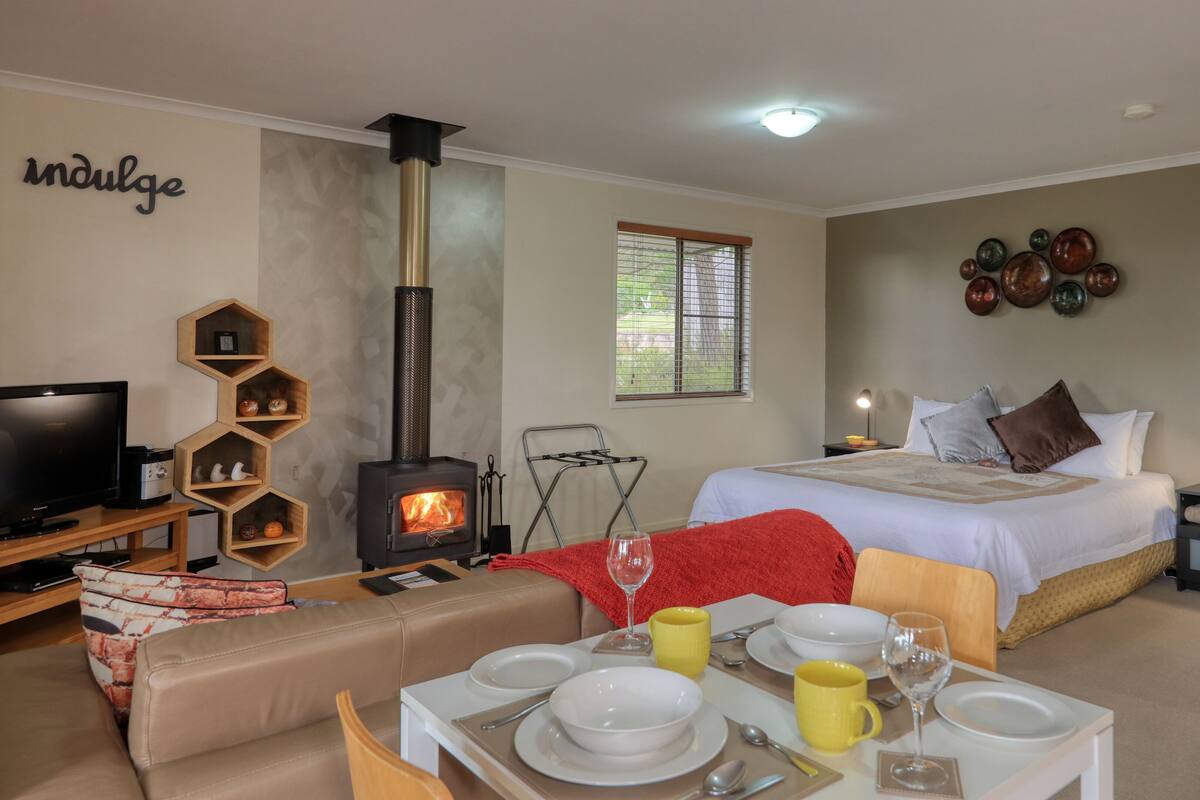 A cozy room with a bed, a TV, a fireplace, and a dining area set up with plates and glasses.