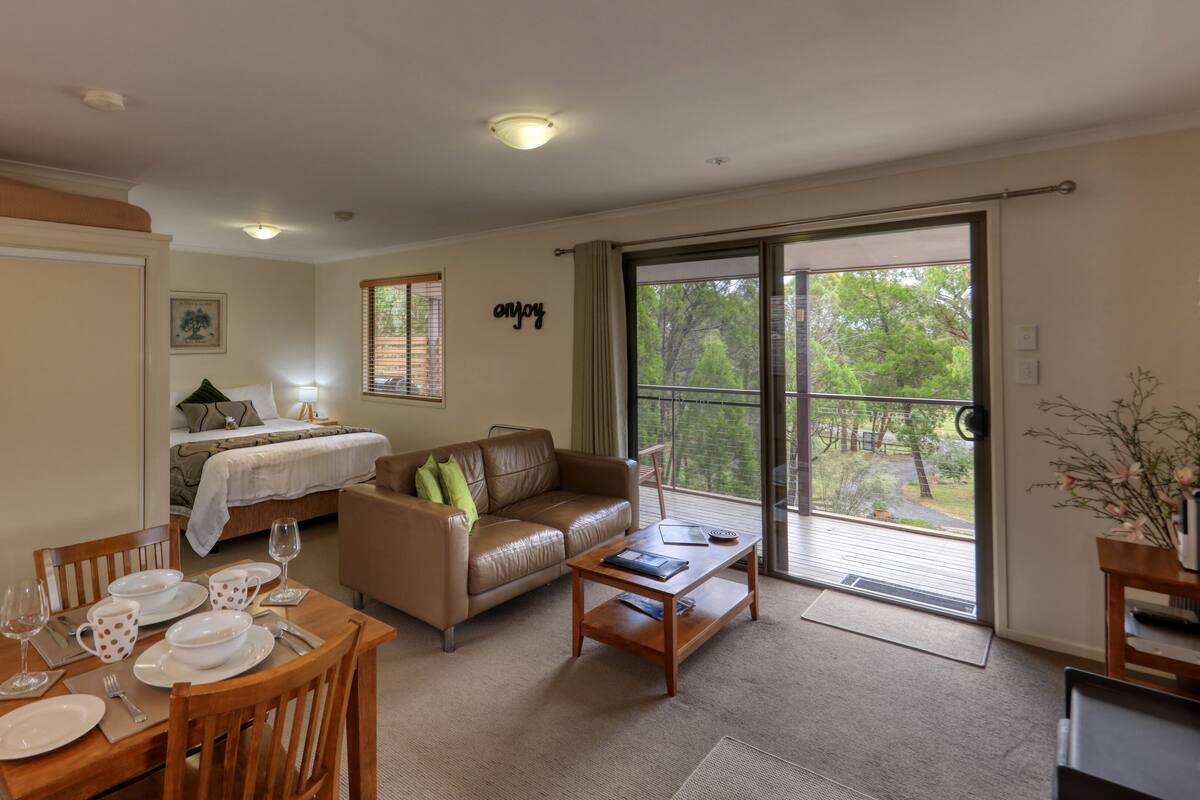 A spacious living area with a dining table set for four, a sofa, and a bed with a view of the outdoors.