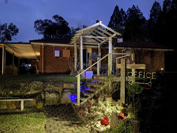 A house with a covered porch, a brick exterior, and a garden with a pathway leading to the entrance.