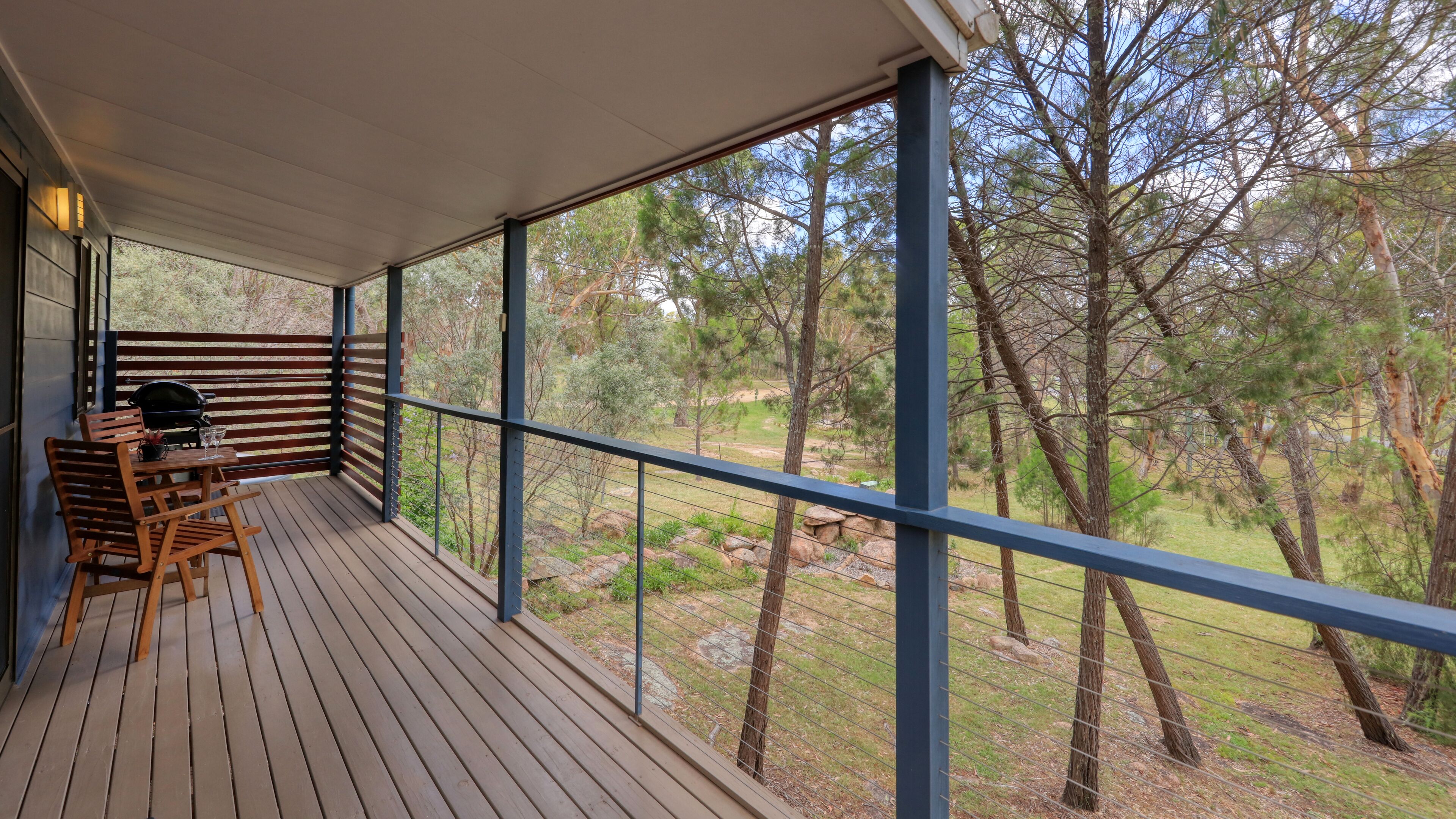 A wooden deck with a table and chairs, overlooking a natural landscape with trees and rocks.
