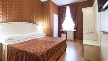 A hotel room with a large bed, a dresser, a window with curtains, and a radiator.