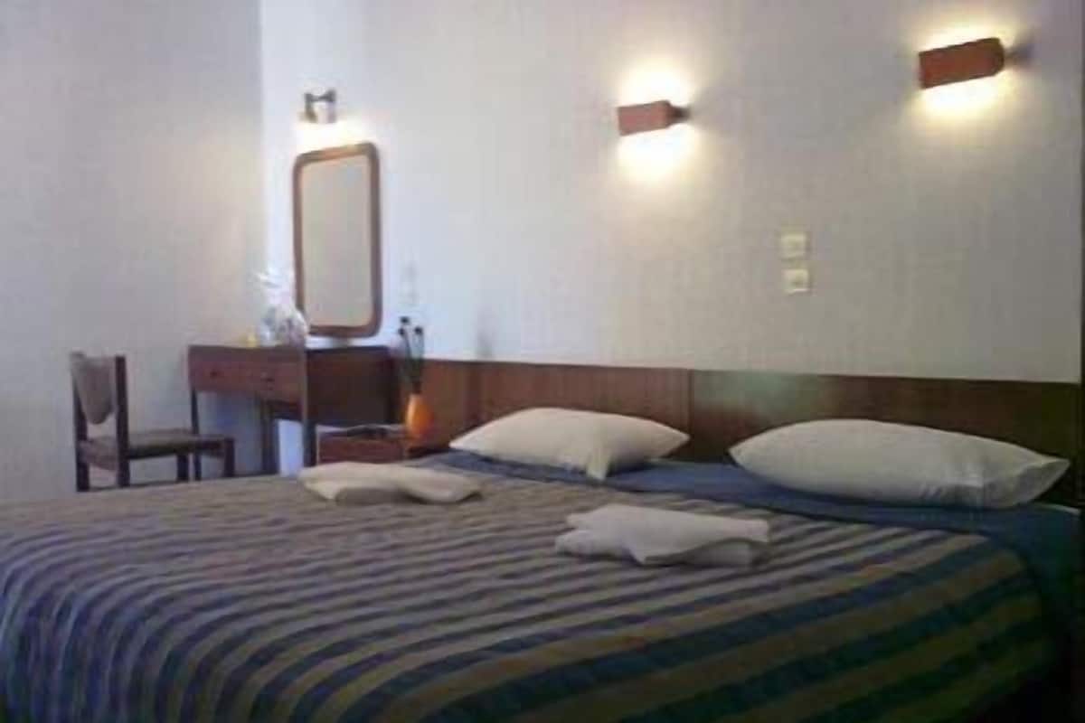 A hotel room with a bed, a bedside table, a chair, and a wall-mounted mirror.