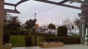 A covered outdoor area with a tiled floor, a seating area with benches, and a view of a parking lot and trees in the background.