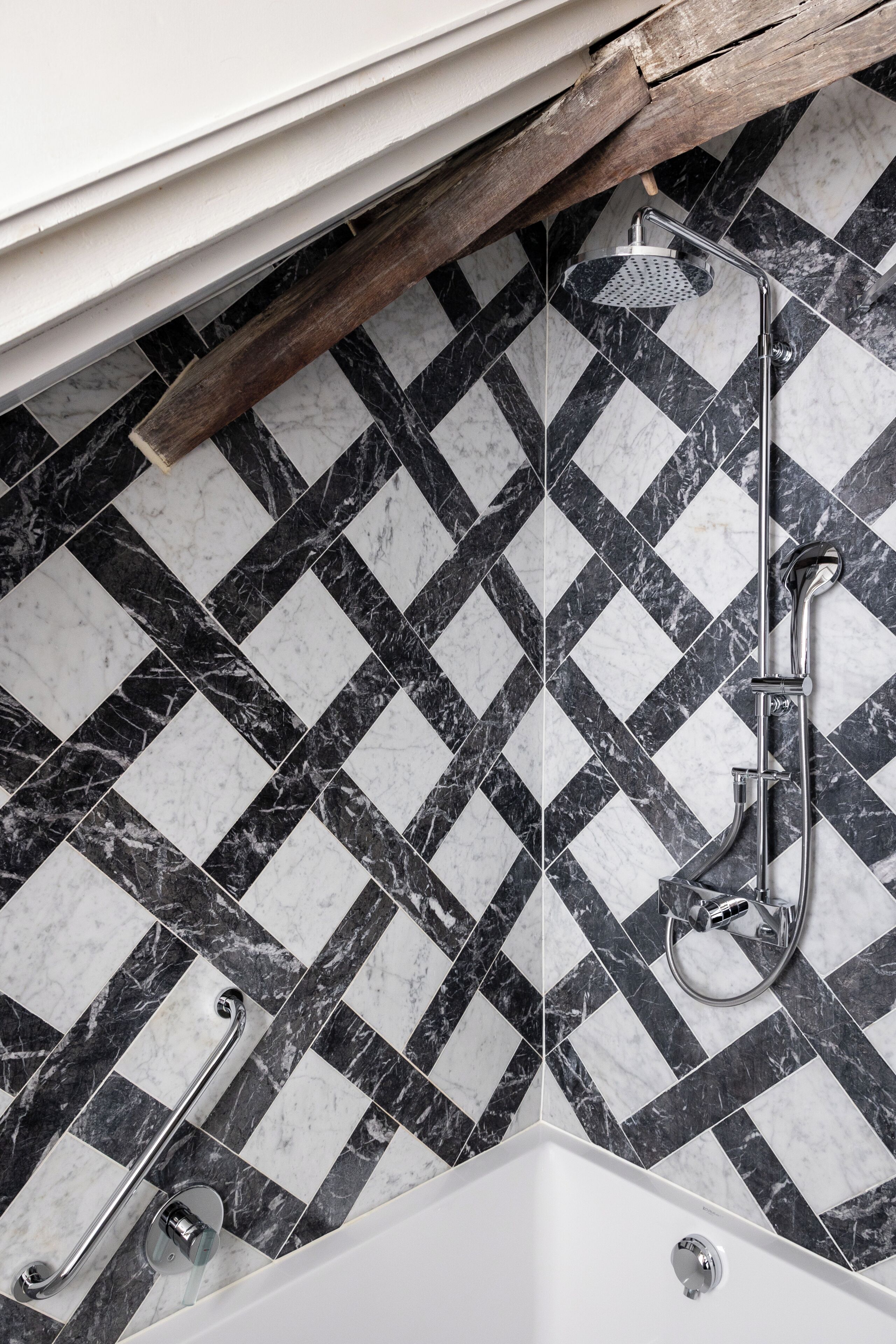A bathroom with a black and white marble tile pattern, a shower with a handheld showerhead, and a grab bar.